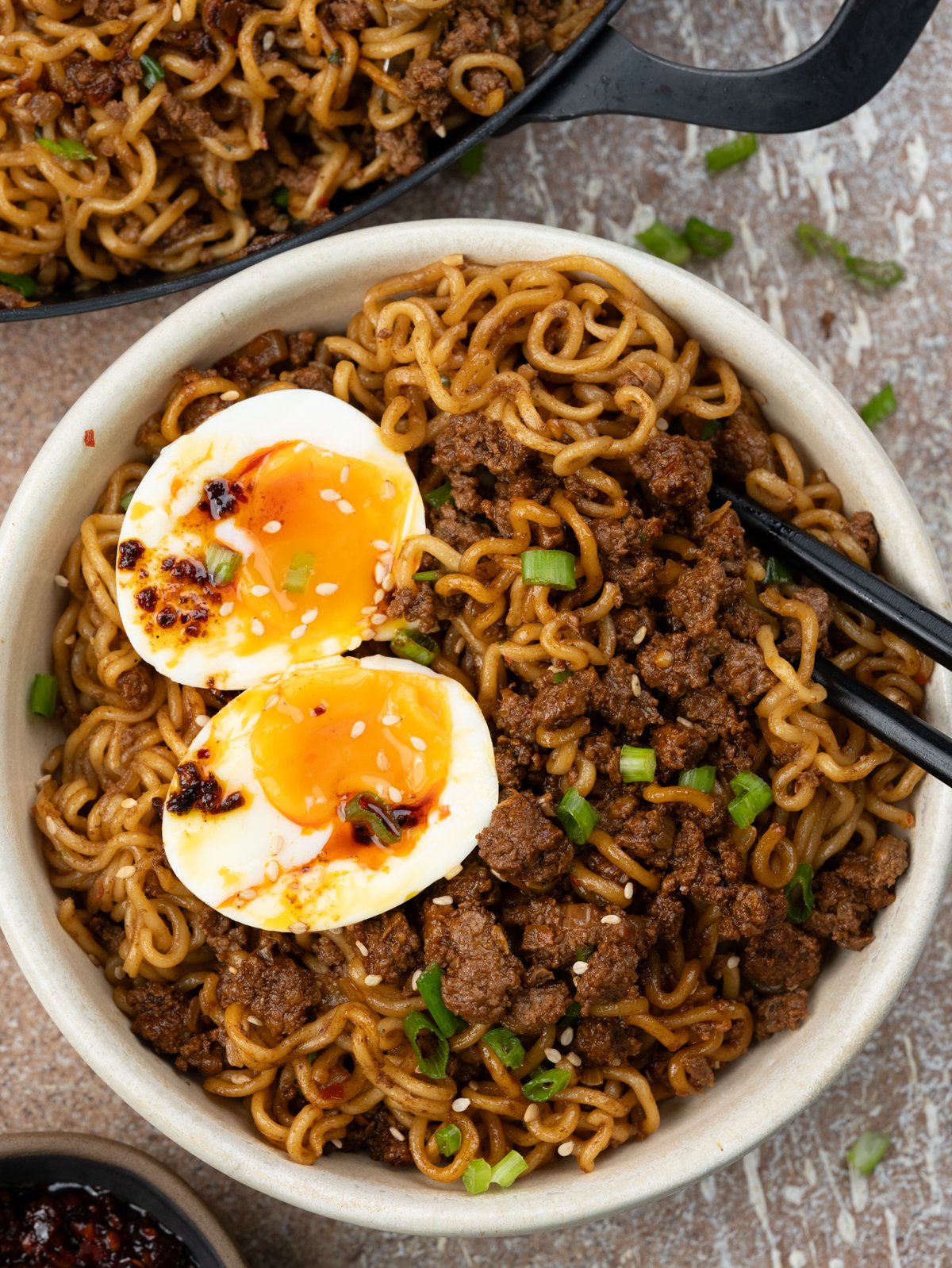 Bowl of Ground beef ramen noodles stir fry topped with jammy eggs, and drizzle of chilli crisp