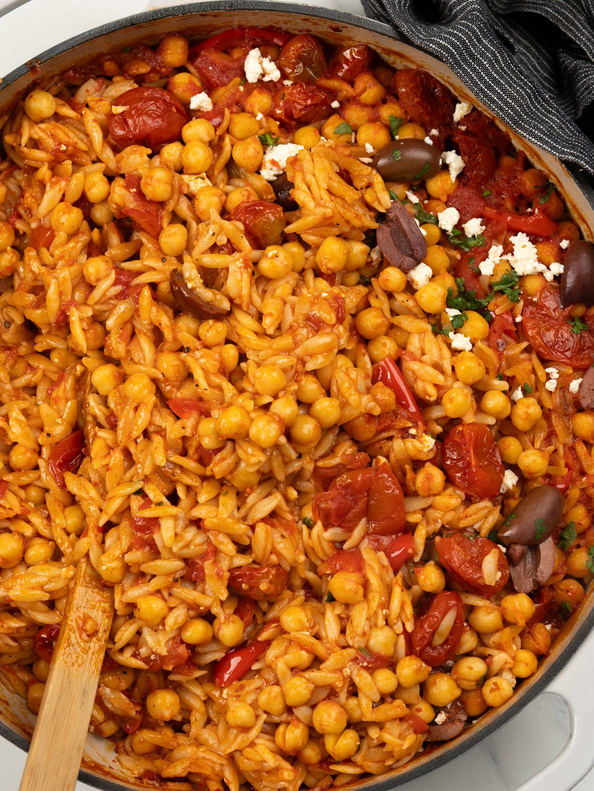 Skillet of baked orzo in cherry tomato, chickpeas and topped with feta and olives