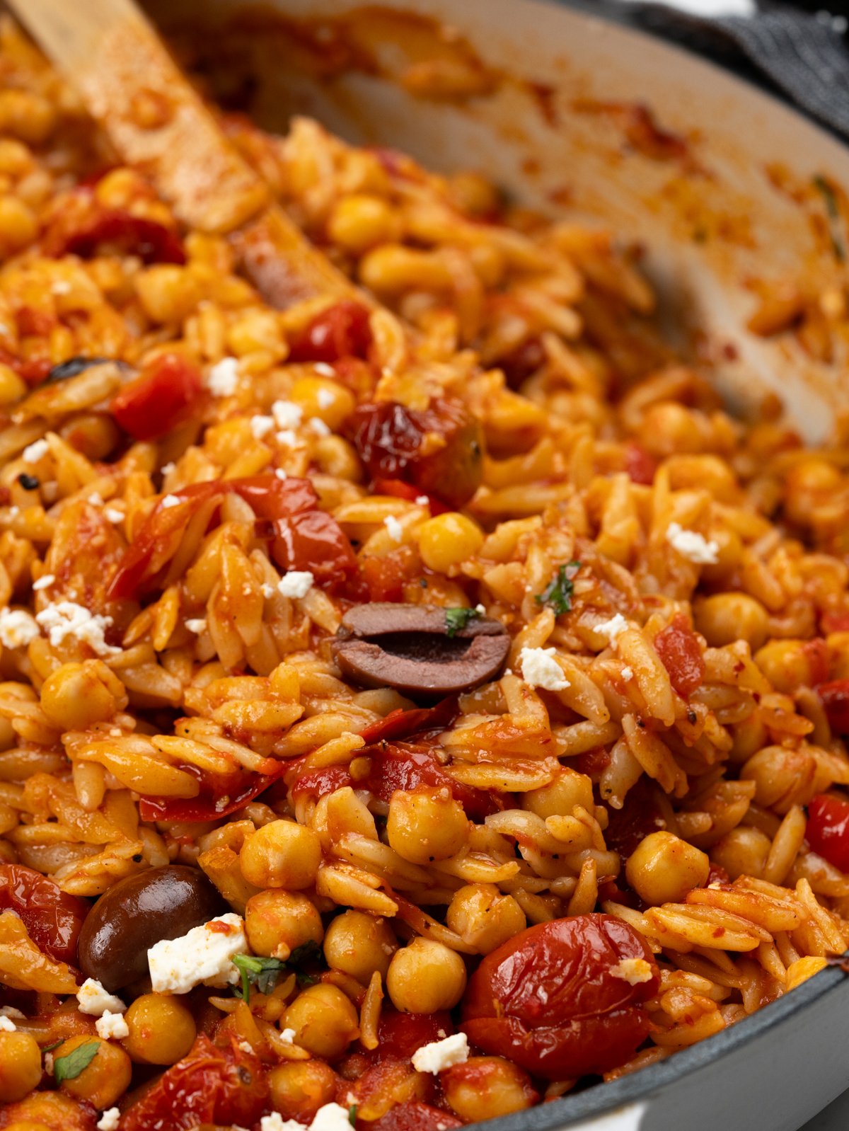 Close up of  baked orzo in cherry tomato, chickpeas and topped with feta and olives