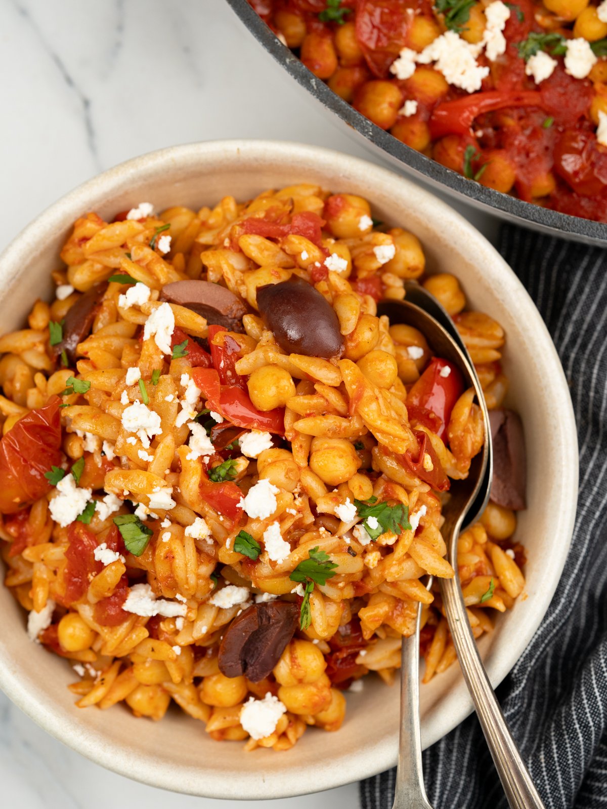 Bowl of baked orzo in cherry tomato, chickpeas and topped with feta and olives