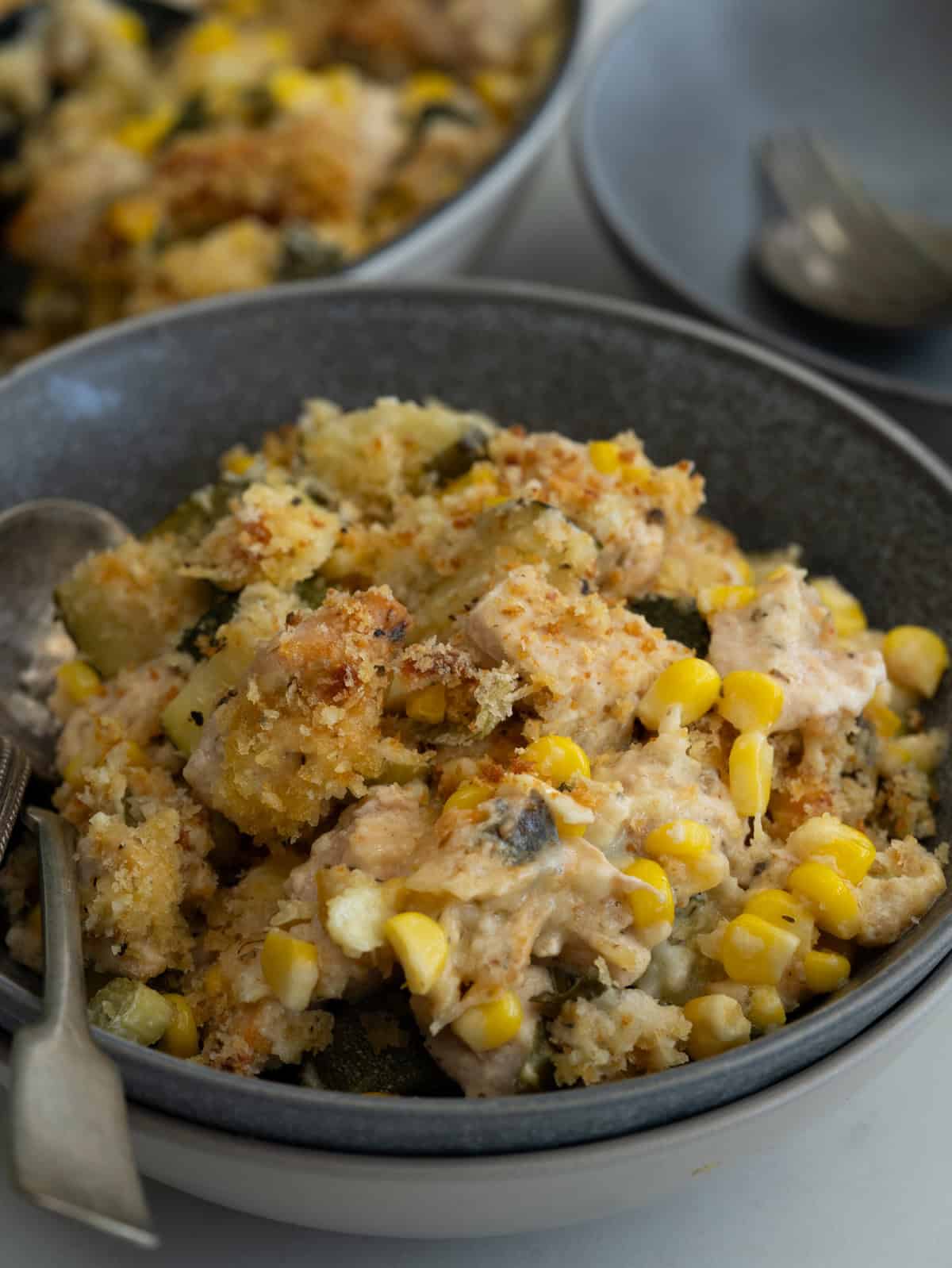 Chicken pieces, zucchini, corn in a creamy cheesy sauce and crunchy bread topping served in a bowl.